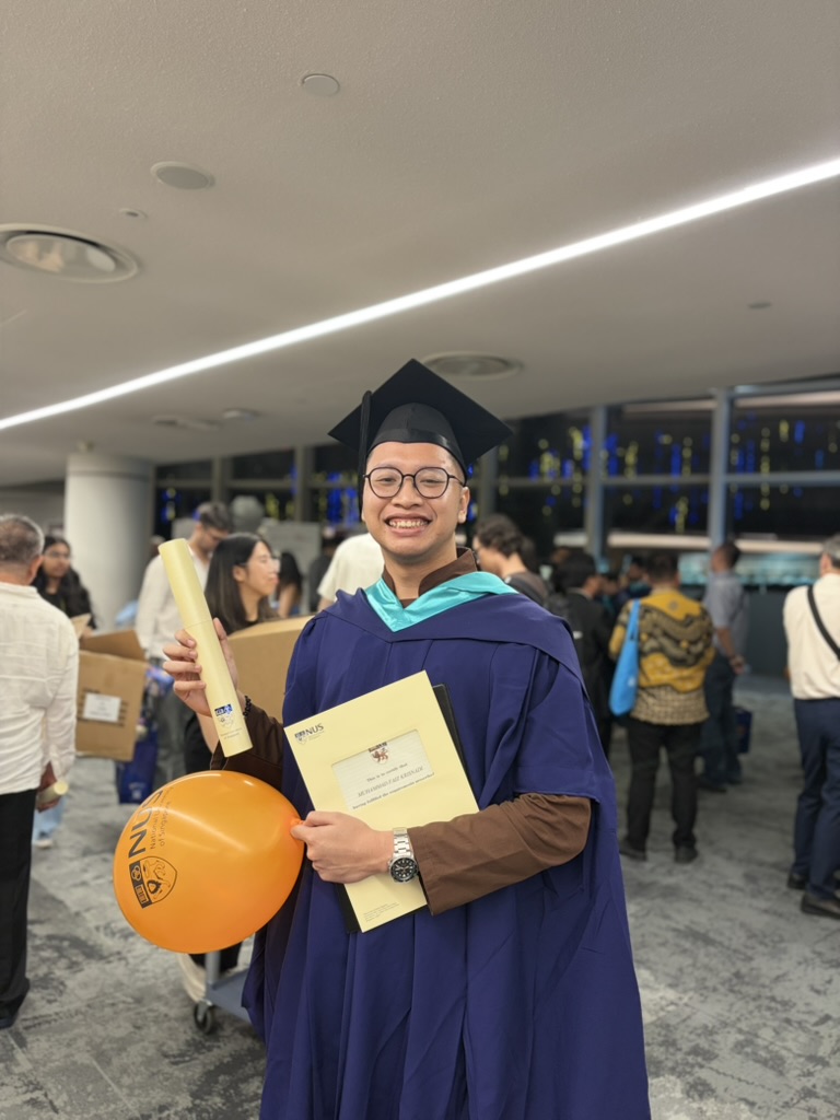 Faiz smiling in graduation robes at NUS